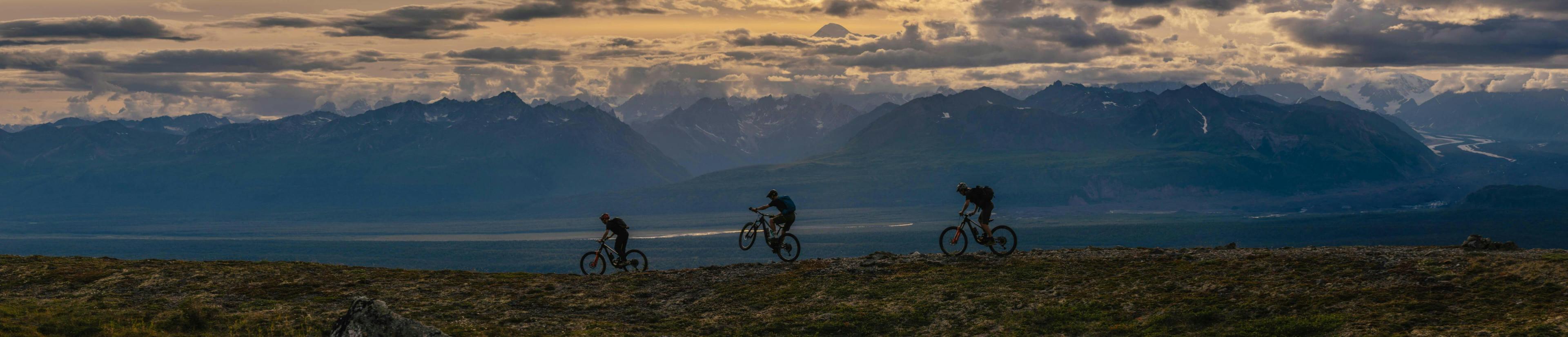 Three riders riding along a ridge line and sunset.